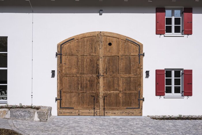 Altes Holztor in der weiß verputzten Fassade, daneben ein Fenster mit roten Läden