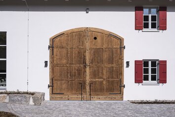 Altes Holztor in der weiß verputzten Fassade, daneben ein Fenster mit roten Läden