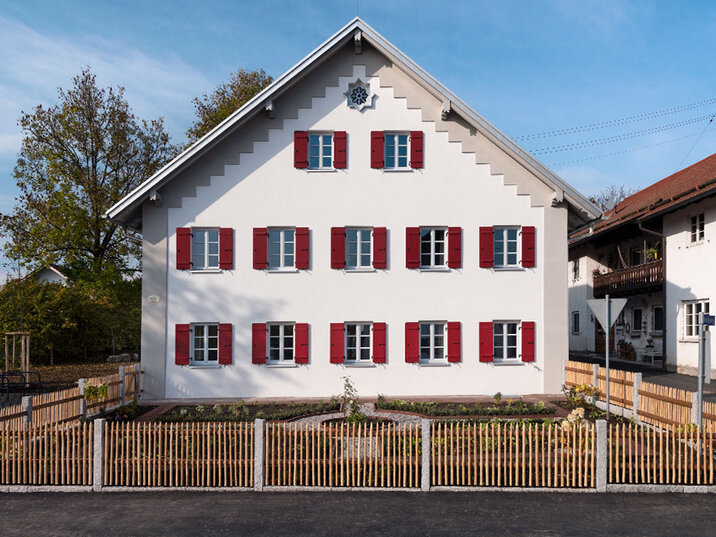 Giebelseite nach der Sanierung: frisch verputzte Fassade mit roten Fensterläden