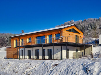 Haus WM von außen: Holzfassade mit Balkon vor verschneiter Landschaft