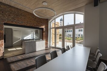 Küchentheke aus Beton neben langer Tafel, Blick durch das Rundbogenfenster ins Freie