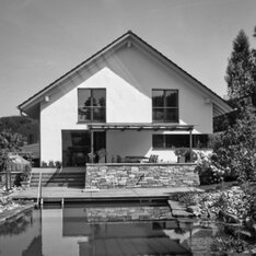 Neubau eines Passivhauses mit Satteldach und Natursteinsockel am Teich, Schwarzweißaufnahme