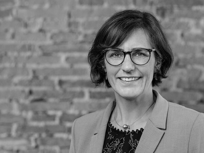 Christine Kirchberger, Architektin, Schwarzweißporträt vor einer Ziegelwand