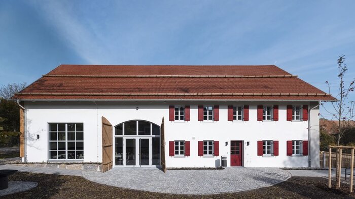 Dorfgemeinschaftshaus Gutenberg von vorn: weiße Fassade mit roten Fensterläden und Rundbogentür